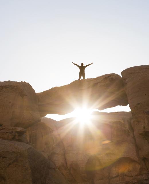Low angle view of woman standing with her arms outstretched on a natural rock bridge in the desert.